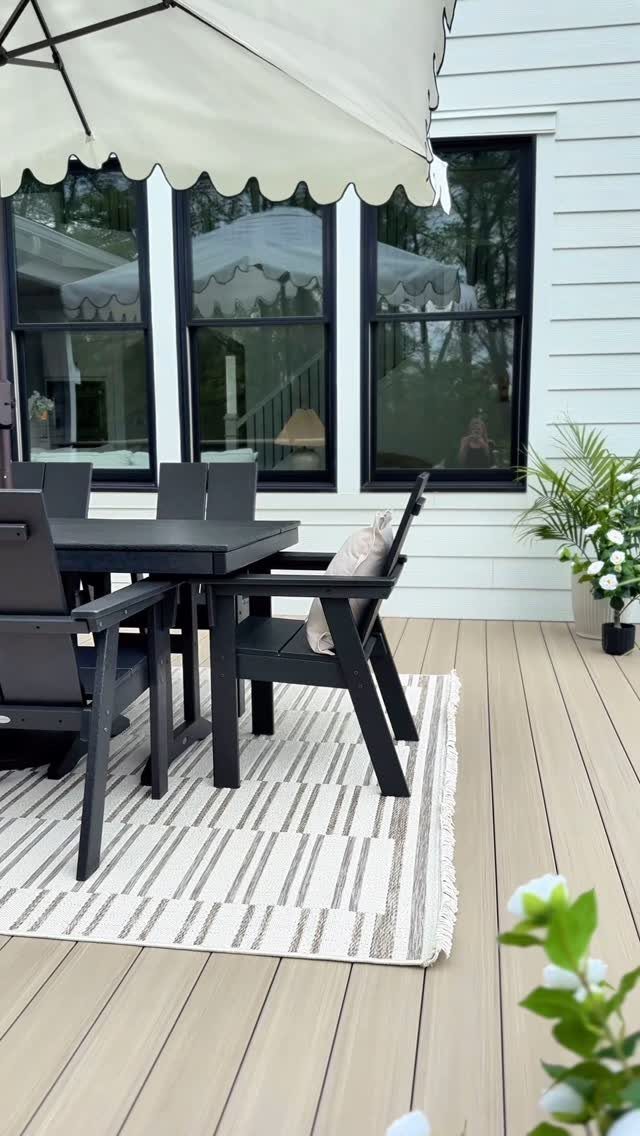 Black outdoor dining set placed on a striped rug on a wooden deck under an umbrella.