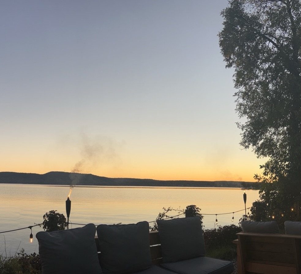 Tiki torches on a string hanging over a deck overlooking a lake at sunset.
