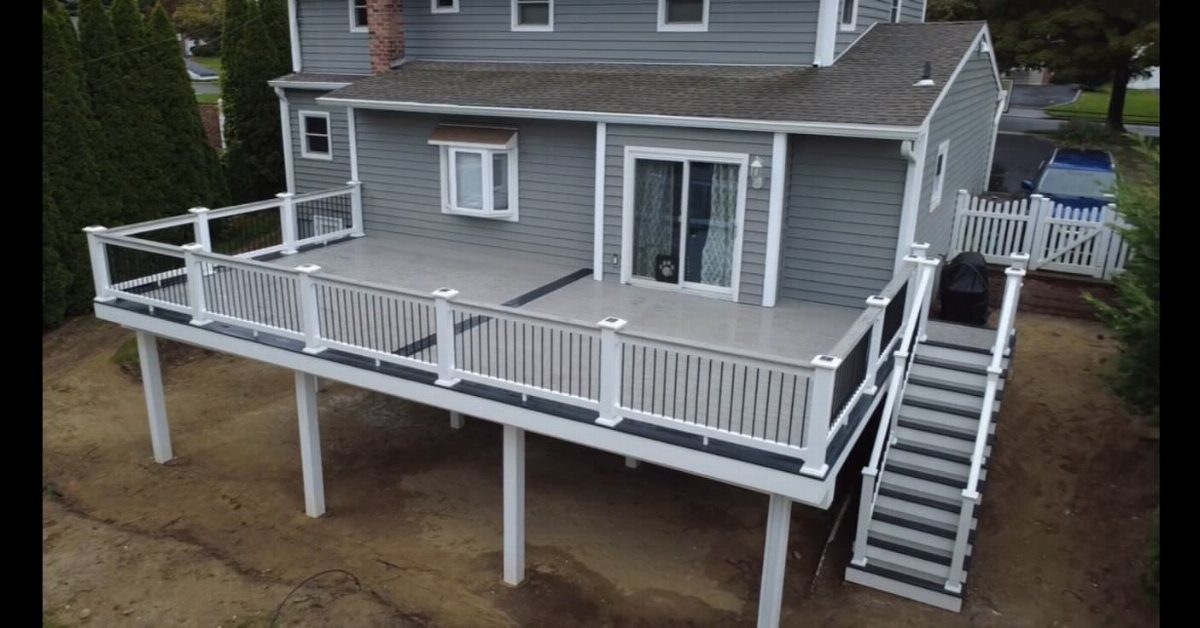 A large grey composite deck with white railings attached to the back of a grey house.
