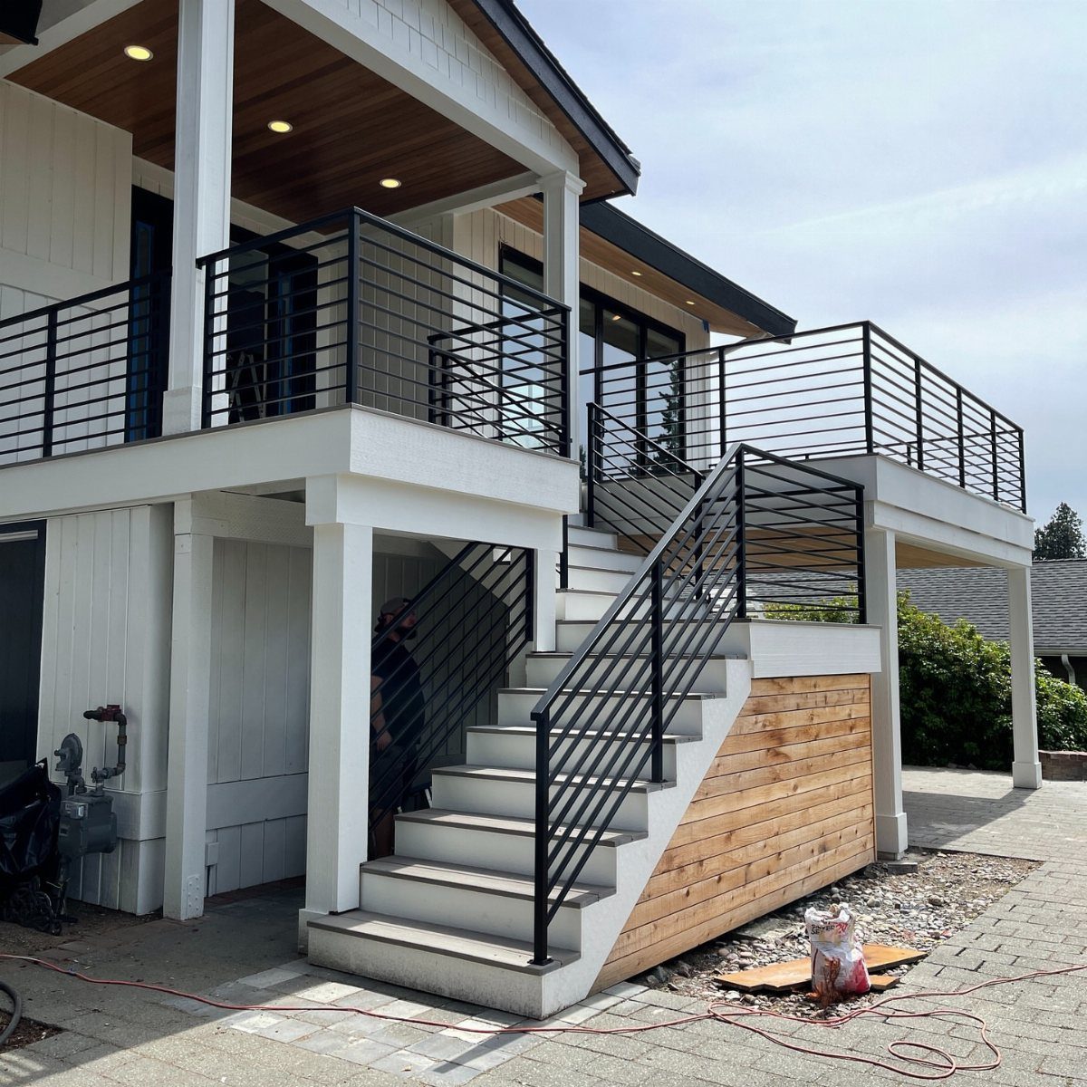 Modern white second-story deck with black metal railings and concrete stairs leading to a patio.