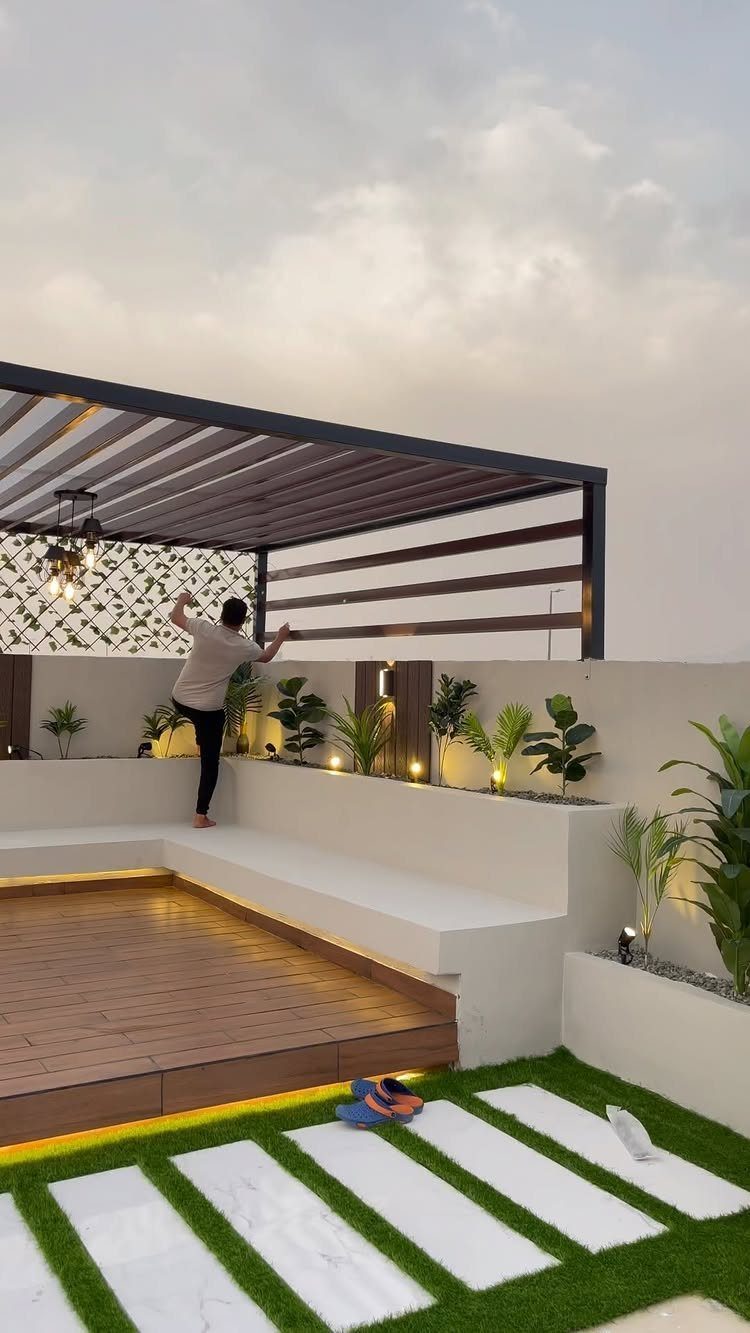 Modern rooftop courtyard with wooden decking, white built-in seating, and stone pavers in green turf.
