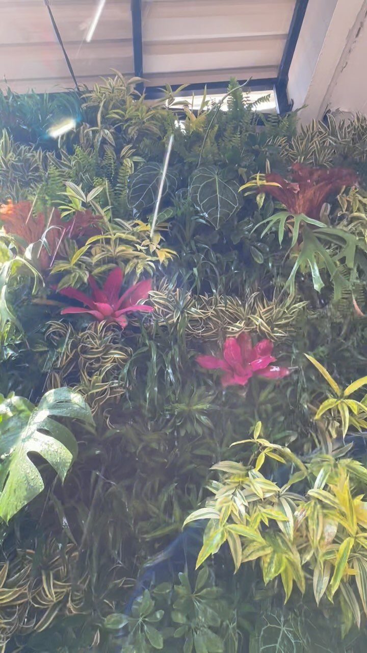 Lush green plants and pink flowers arranged in a dense vertical living wall.