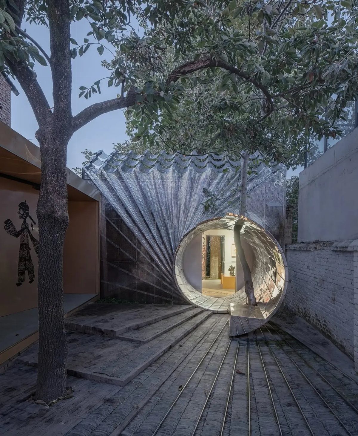 A sculptural circular tunnel structure integrated with a tree in a modern urban courtyard setting.