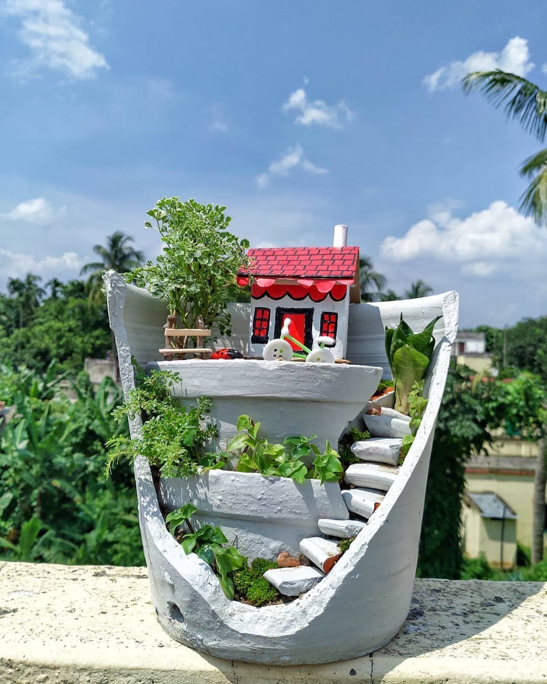 8 DIY Garden Projects for Fairy Gardens, Raised Beds and Outdoor Play 2 A broken grey pot transformed into a miniature fairy garden with a small house and greenery.