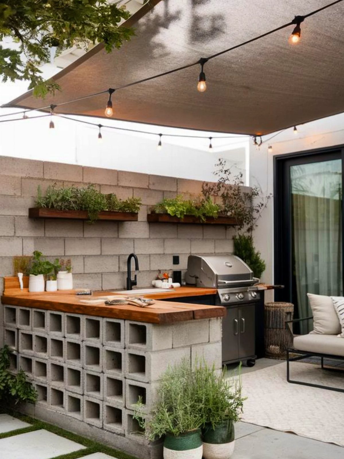 Cinder block base supporting a wooden countertop in an outdoor kitchen with a grill and sink.