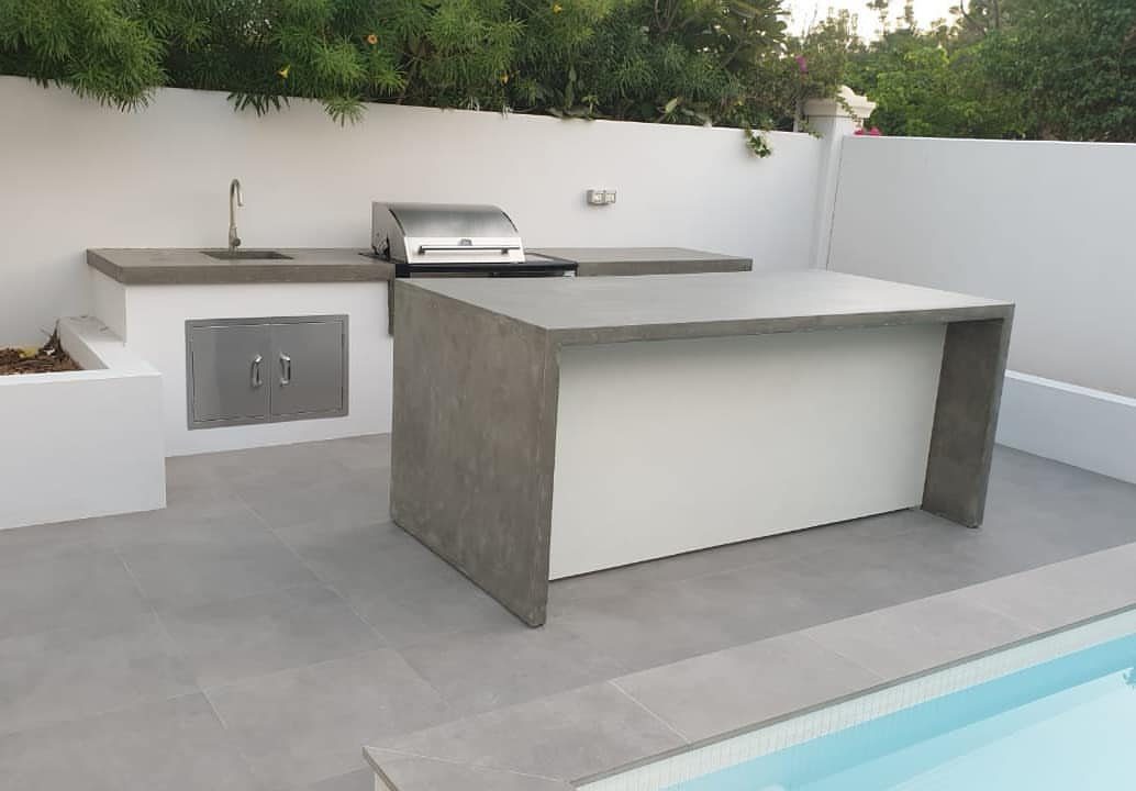 Concrete countertops on an outdoor kitchen island and grill station next to a swimming pool.