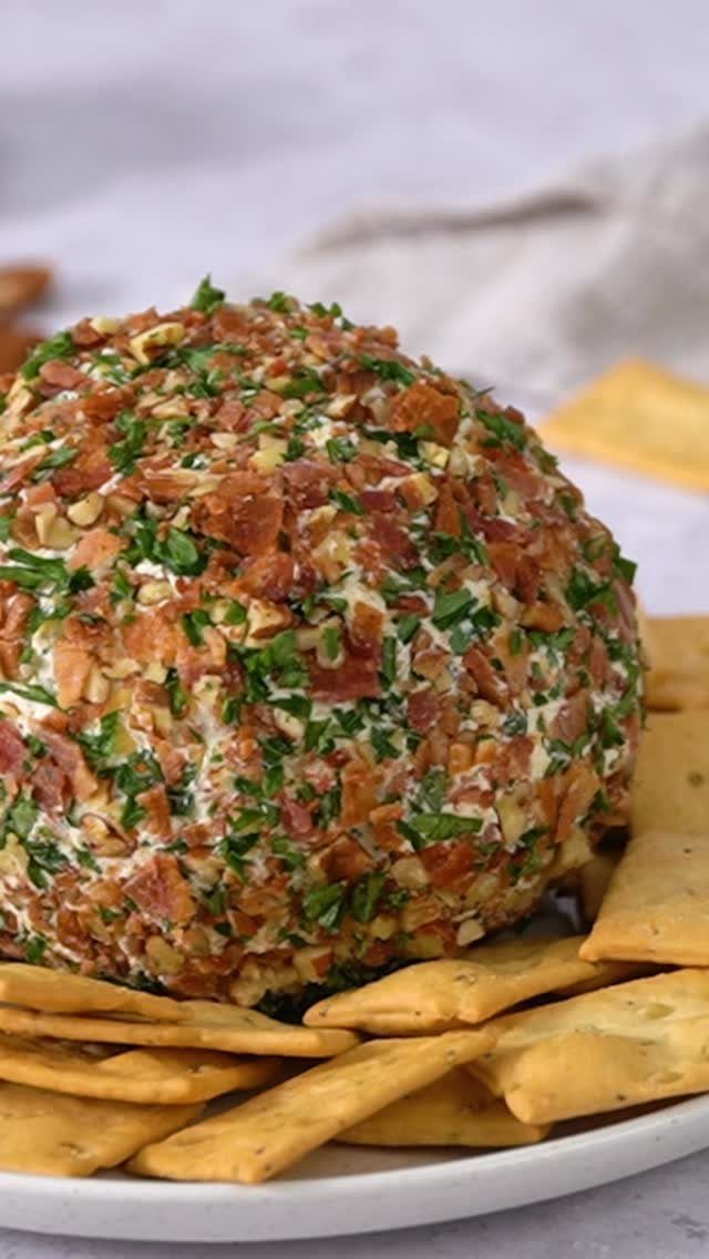 32 Easy Christmas Party Ideas for Food, Drinks, and Hosting in 2026 29 A large cheese ball covered in bacon and herbs surrounded by crackers on a plate.