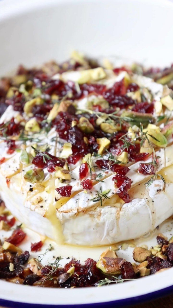 32 Easy Christmas Party Ideas for Food, Drinks, and Hosting in 2026 2 Baked brie topped with dried cranberries, pistachios, and fresh thyme in a white dish.