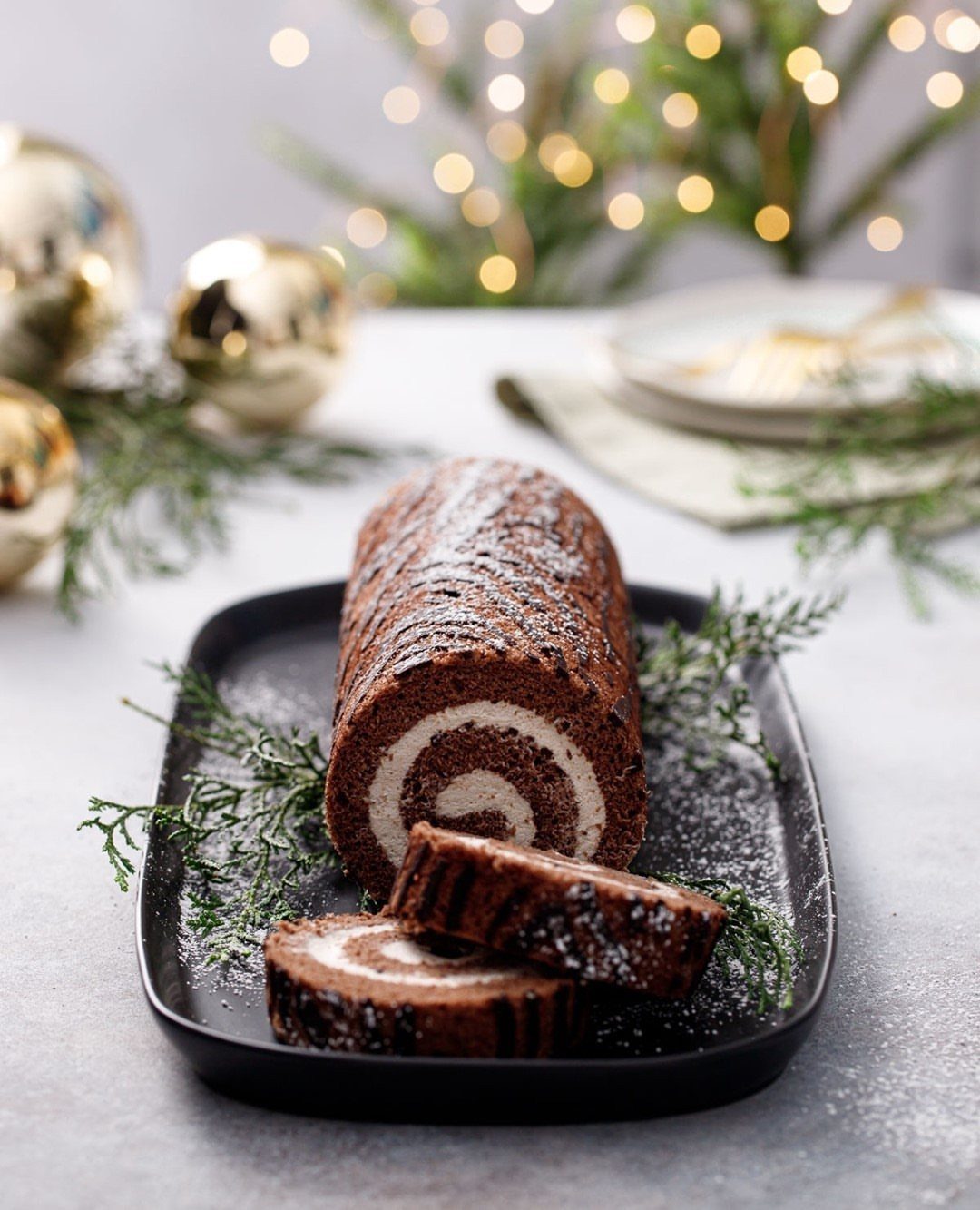 32 Easy Christmas Party Ideas for Food, Drinks, and Hosting in 2026 24 Chocolate roll cake with white cream filling on a black platter with festive decorations.