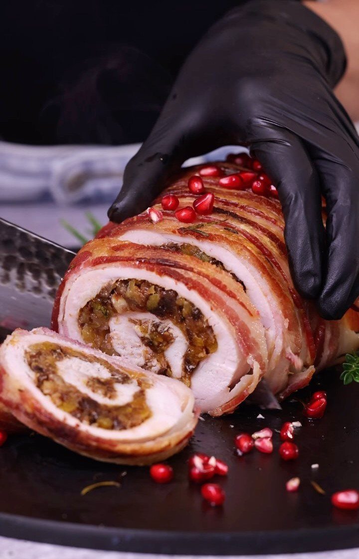 32 Easy Christmas Party Ideas for Food, Drinks, and Hosting in 2026 21 Sliced bacon-wrapped turkey breast roll with stuffing and pomegranate seeds on a black platter.