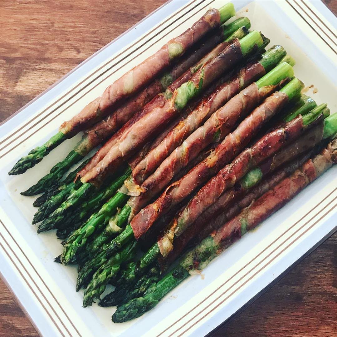 32 Easy Christmas Party Ideas for Food, Drinks, and Hosting in 2026 14 Prosciutto-wrapped asparagus spears arranged on a white rectangular serving platter.