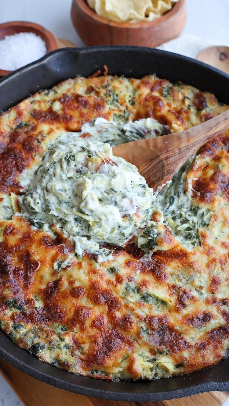 32 Easy Christmas Party Ideas for Food, Drinks, and Hosting in 2026 10 Spinach artichoke dip being scooped from a cast iron skillet with a wooden spoon.