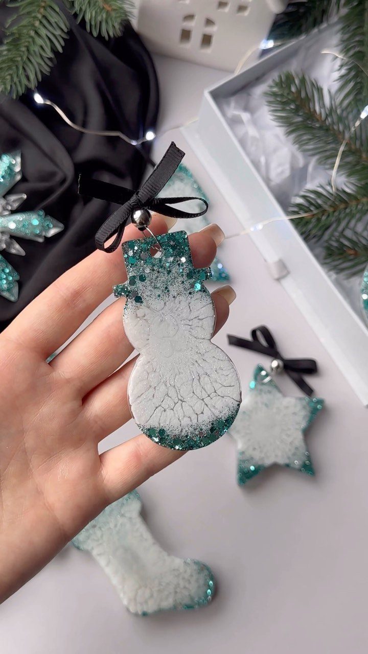 17 Easy DIY Christmas Gifts: Handmade Presents for Every List 11 A hand holding a white and teal glittery snowman ornament with a black ribbon.