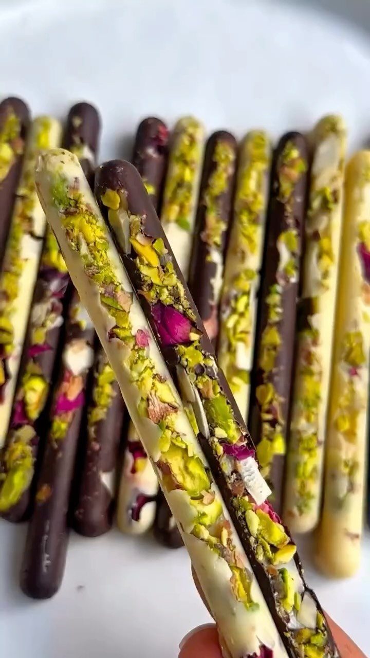 17 Easy DIY Christmas Gifts: Handmade Presents for Every List 15 Chocolate-covered pretzel rods decorated with crushed pistachios and pink rose petals on a white plate.
