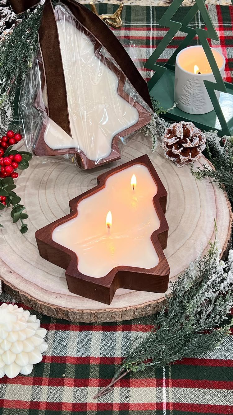 Tree-shaped white candles resting on a wooden slice amidst festive holiday decorations.