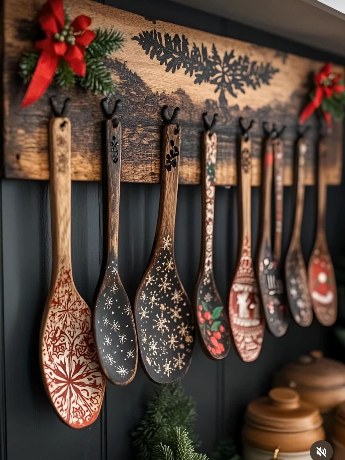 Decorated wooden cooking spoons hanging from a rustic wooden rack against a dark wall.