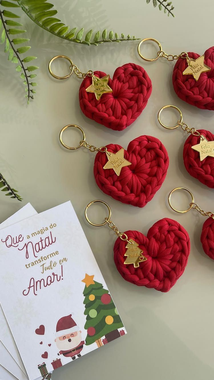 Red crocheted heart keychains with gold charms resting on a surface near a Christmas card.