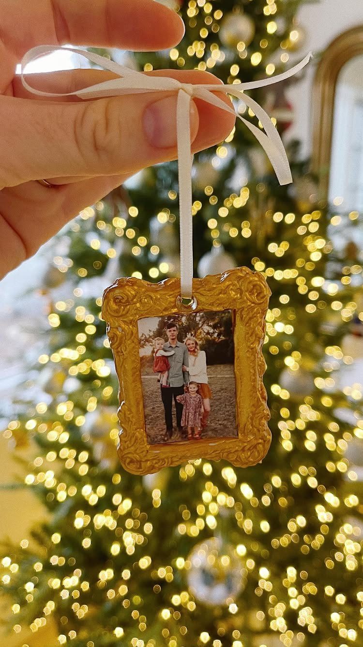 A hand holding a gold framed photo ornament in front of a glowing Christmas tree.