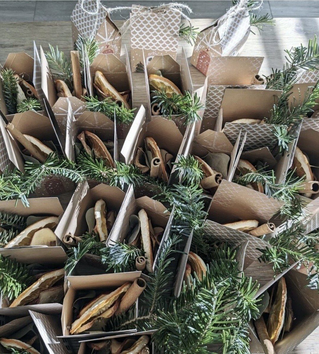 Small brown paper bags filled with dried orange slices and cinnamon sticks nestled among evergreen branches.