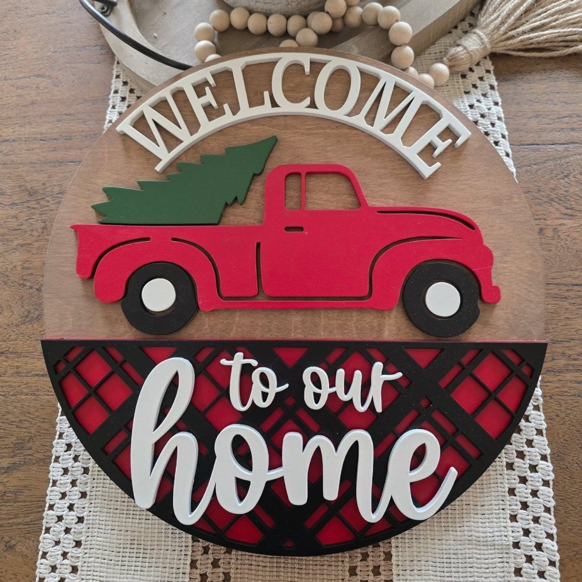 Wooden circular sign with a red truck, Christmas tree, and welcome text on plaid background.