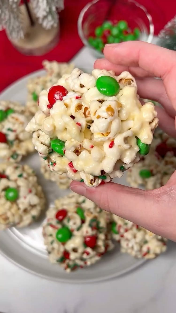A hand holding a white chocolate popcorn ball decorated with red and green candies.