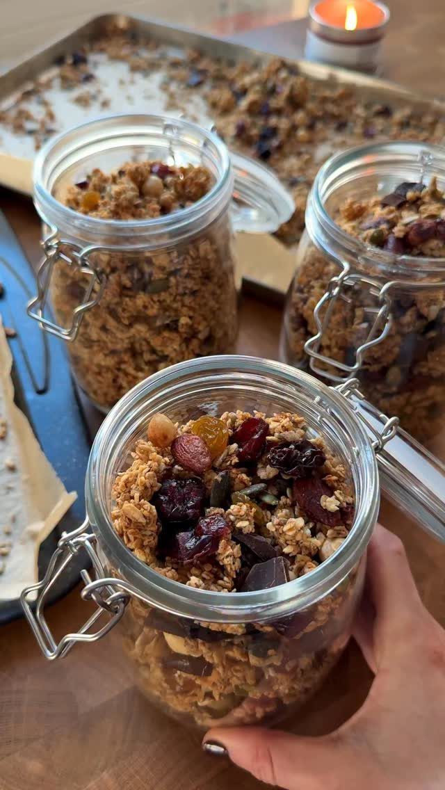 Three glass mason jars filled with granola containing dried fruit on a wooden surface.