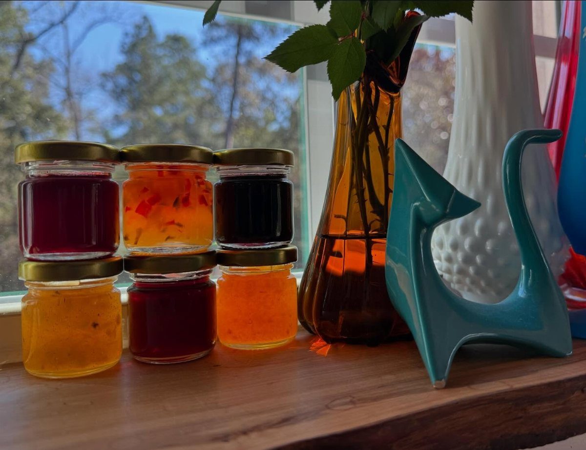 Six small glass jars filled with colorful fruit jams arranged on a wooden windowsill.