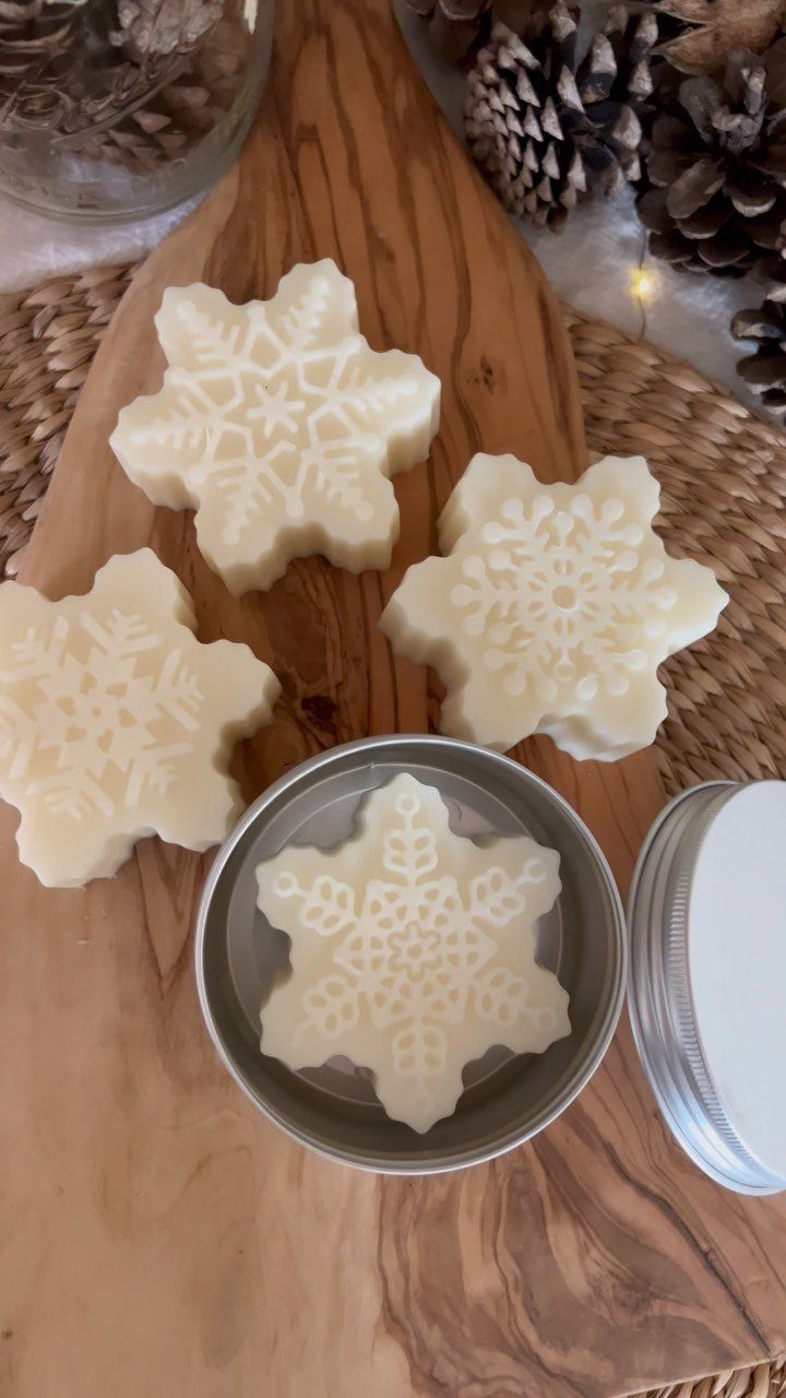 Snowflake shaped white lotion bars on a wooden board next to a metal tin.