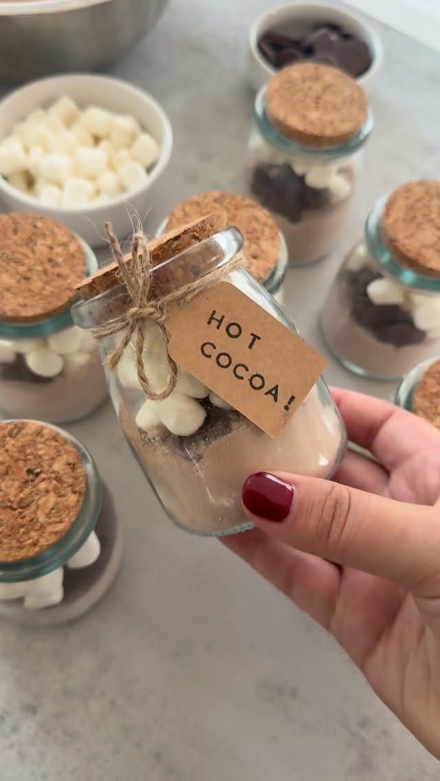 A hand holding a small glass jar filled with layered hot cocoa mix and marshmallows.