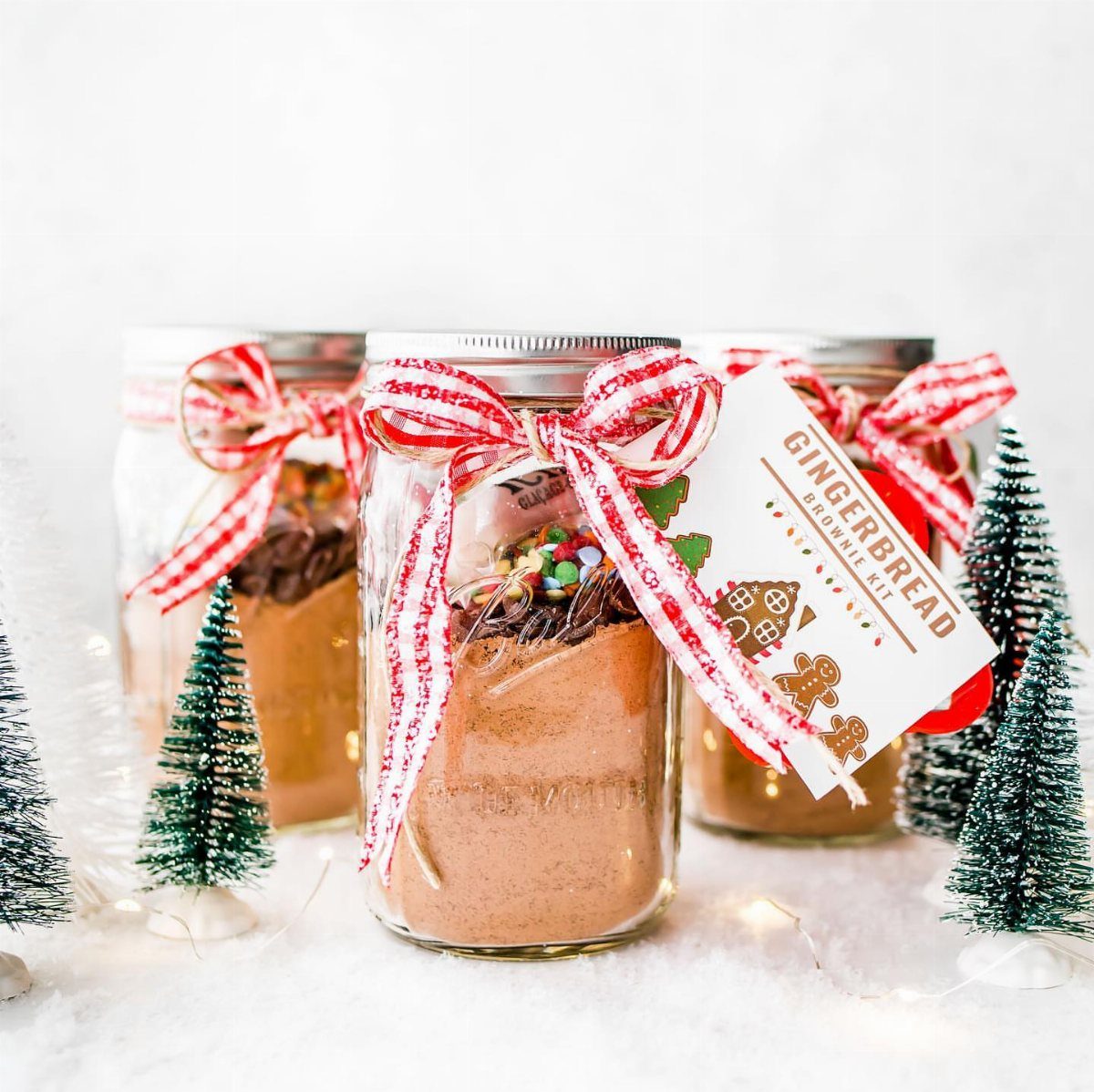 Three mason jars filled with brownie mix, decorated with red striped ribbons and festive tags.