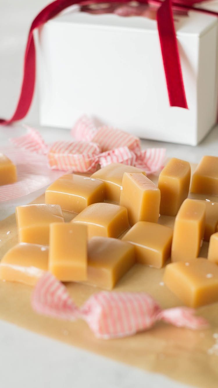 Golden caramel candy squares scattered on a surface with some wrapped in red and white striped paper.