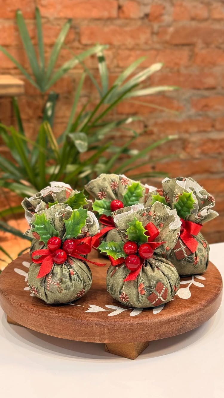 Four festive fabric scented sachets with red ribbons and berries on a wooden tray.