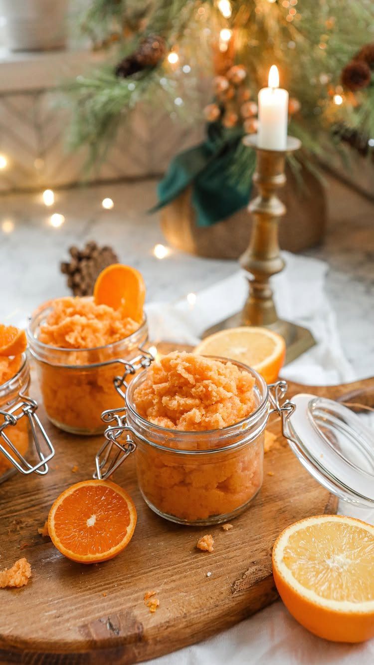Two glass jars filled with orange sugar scrub on a wooden board with citrus slices.