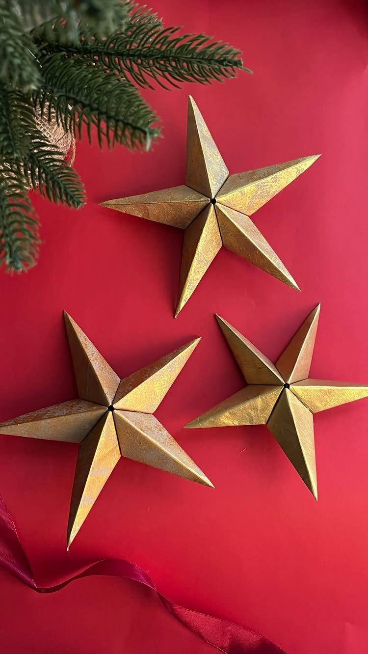 Three gold 3D paper stars resting on a red background with pine branches.