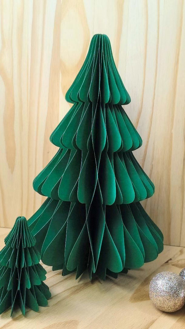 Two green accordion-style paper Christmas trees standing on a light wooden surface.