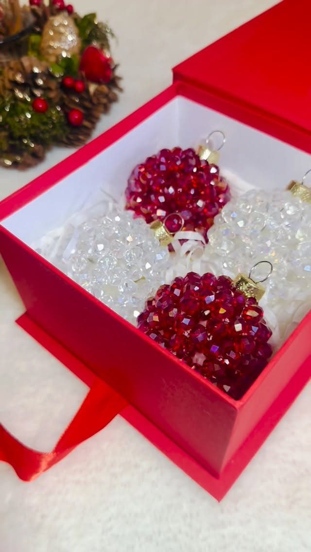 Red and clear beaded Christmas ornaments inside a red gift box with white tissue paper.