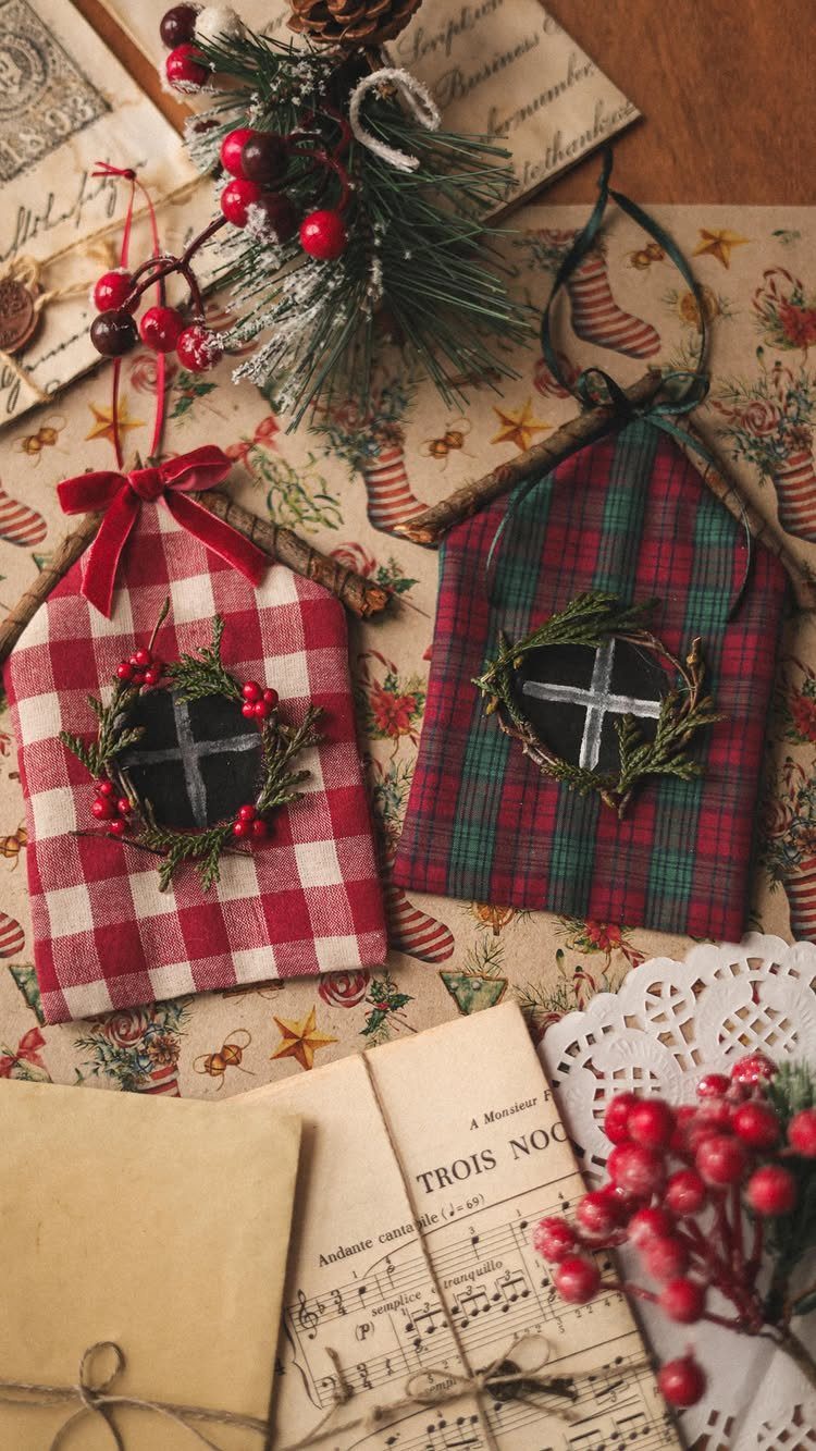 Two fabric house-shaped ornaments with small window designs and greenery on patterned paper.