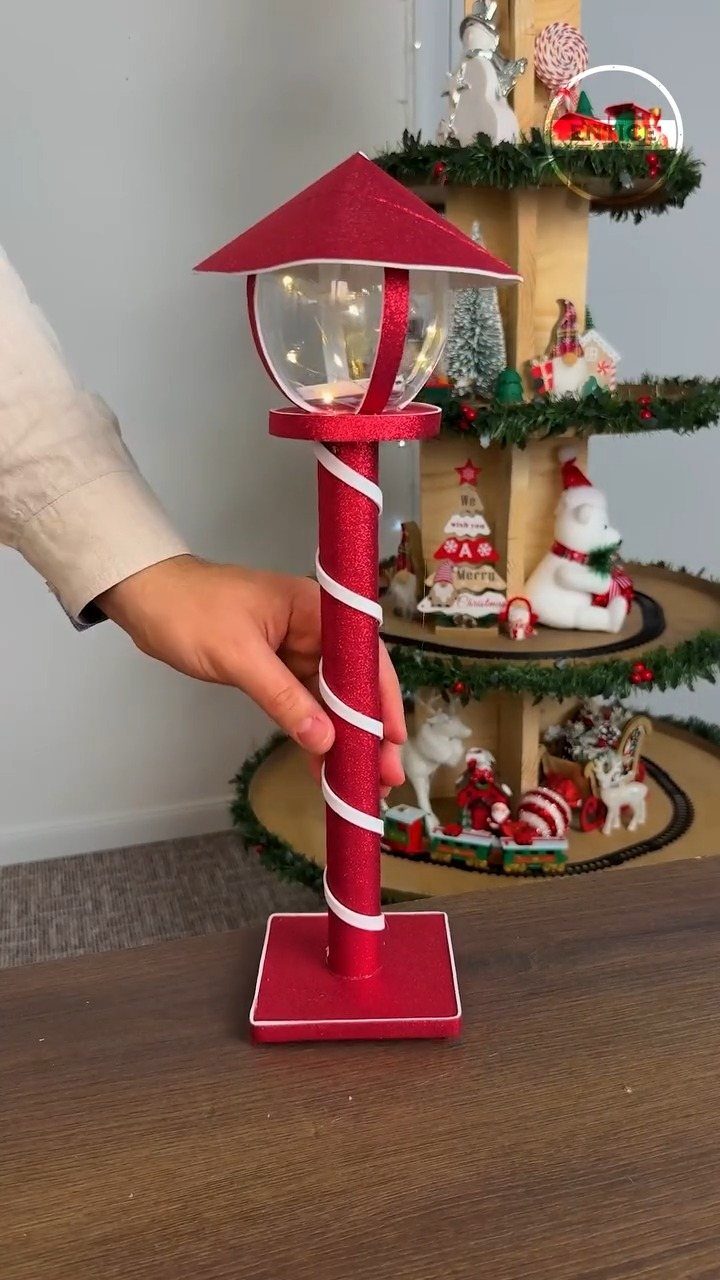 A hand holds a red and white striped DIY Christmas lantern with a clear glass globe top.