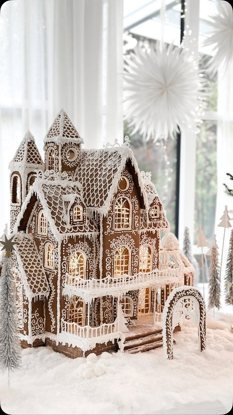A large, detailed gingerbread house decorated with intricate white icing on a snowy surface.