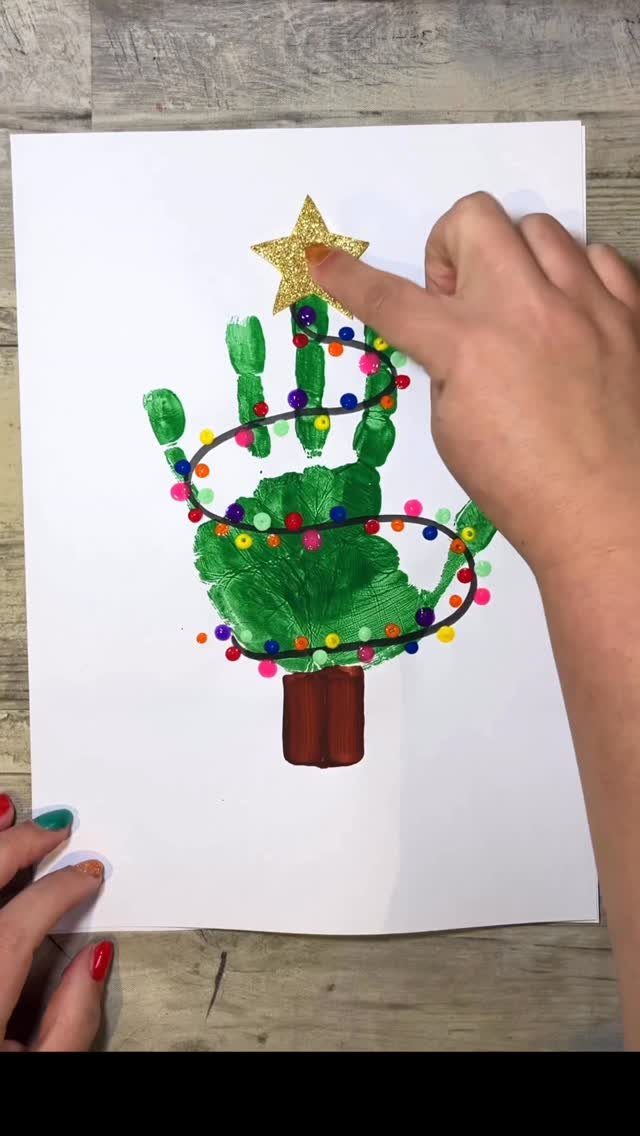 A green handprint Christmas tree with colorful dots and a gold glitter star on white paper.