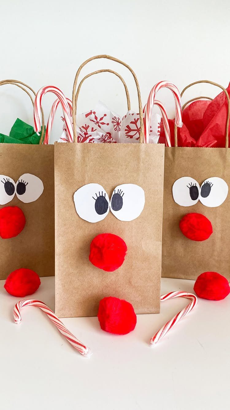 Three brown paper bag reindeer crafts with red pom-pom noses and candy canes on white background.
