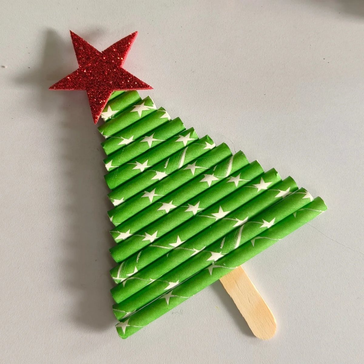 A Christmas tree craft made of green patterned paper straws and a red glitter star.