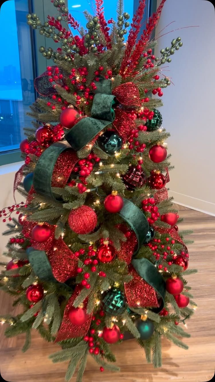 A decorated Christmas tree with red and green ornaments, red berries, and green velvet ribbons.