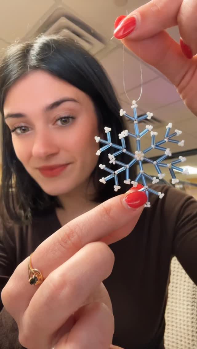 A person holding a blue and white beaded snowflake ornament against a blurred background.