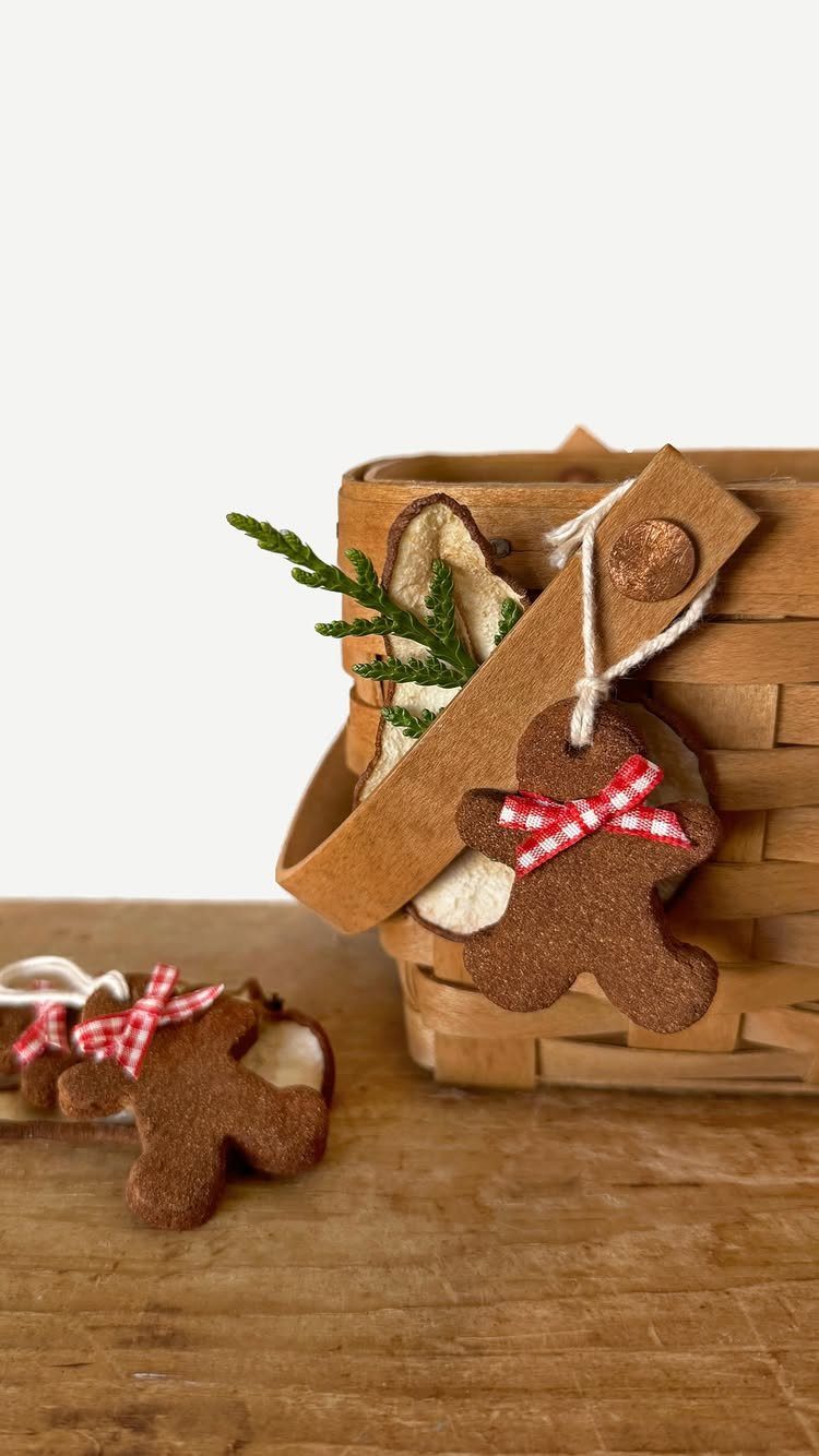 Gingerbread man shaped dough ornaments hanging from a small woven wooden basket on a wooden surface.