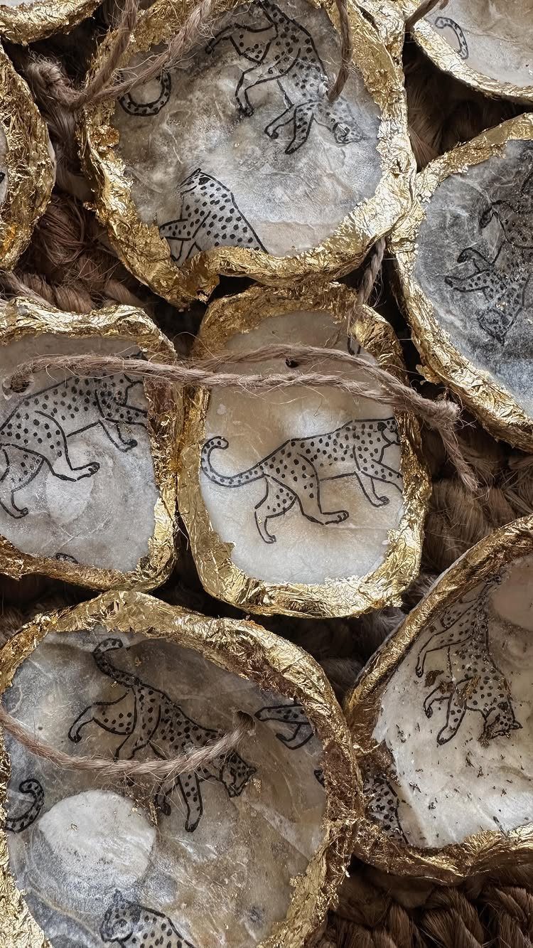 Oyster shell ornaments with gold leaf edges and black ink leopard drawings hanging by twine.