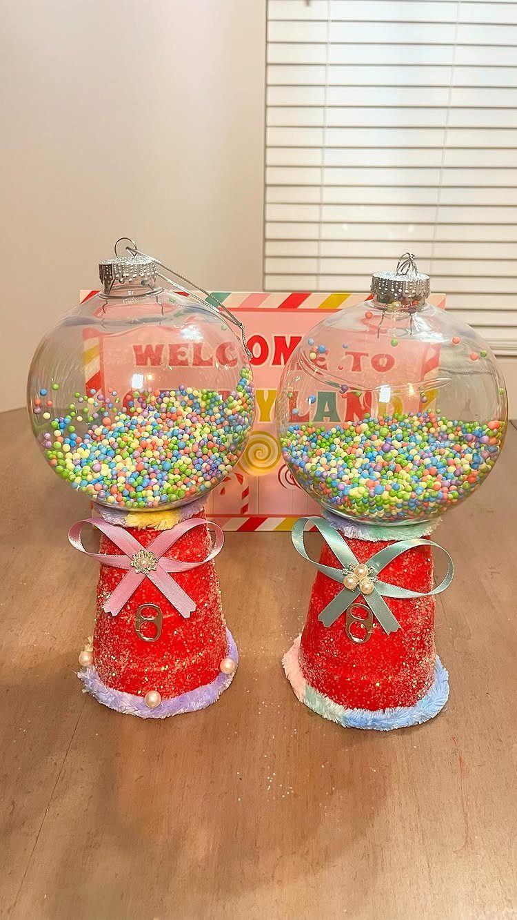Two handmade gumball machine ornaments filled with colorful beads sitting on a wooden table.