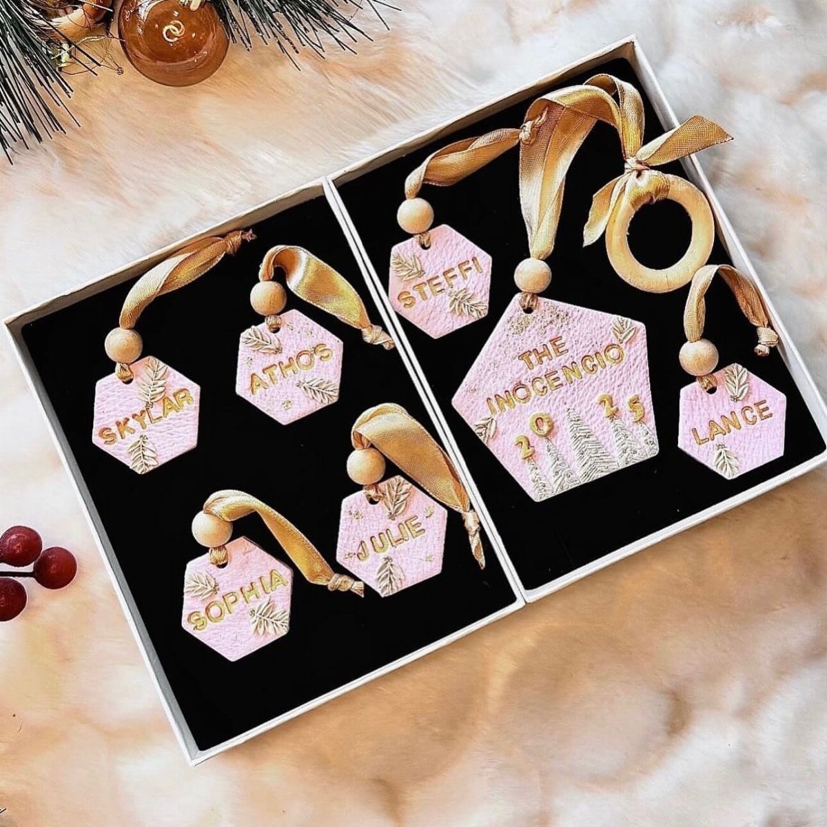 Pink hexagonal polymer clay ornaments with gold names and white trees in gift boxes.