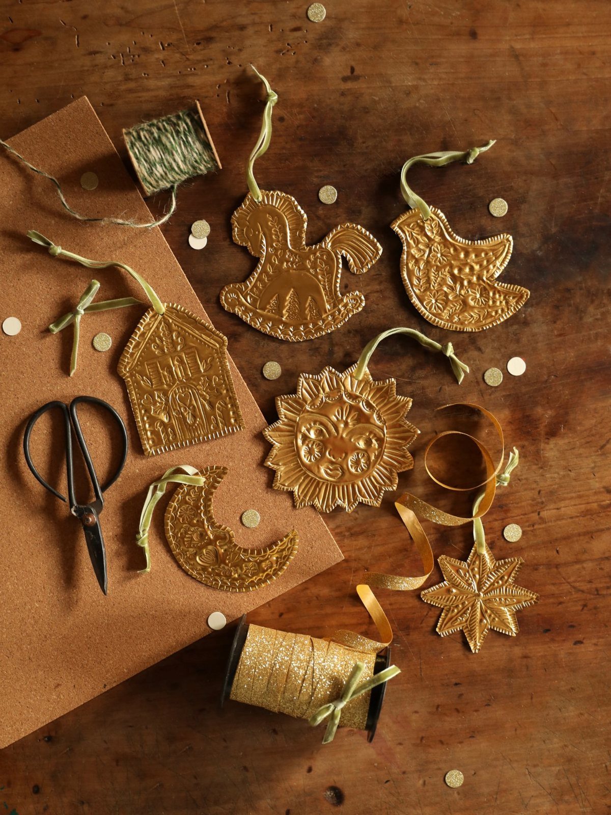 Gold embossed ornaments in various shapes scattered on a wooden table with scissors and gold ribbon.
