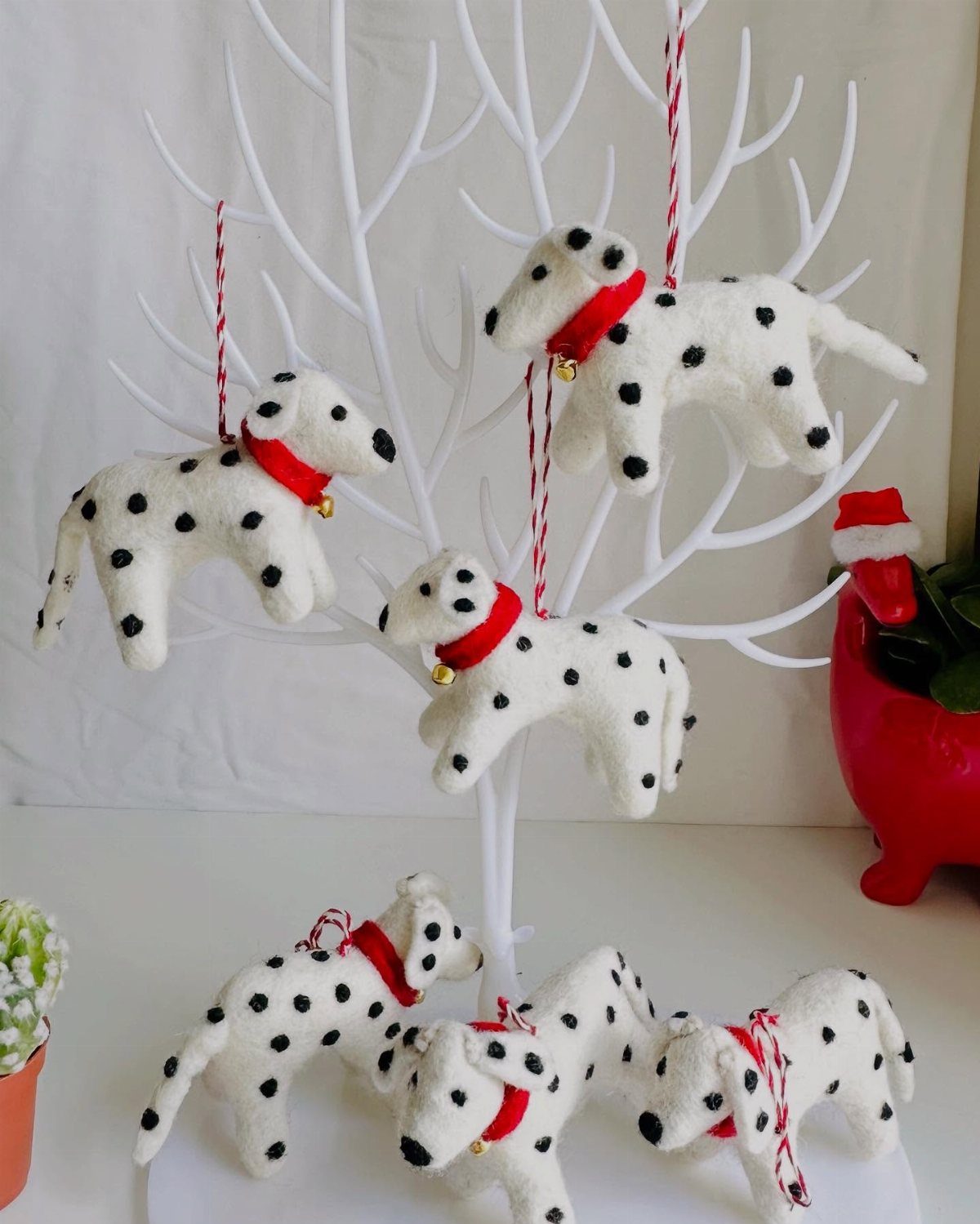 White felt Dalmatian dog ornaments with red collars hanging from a white decorative branch tree.